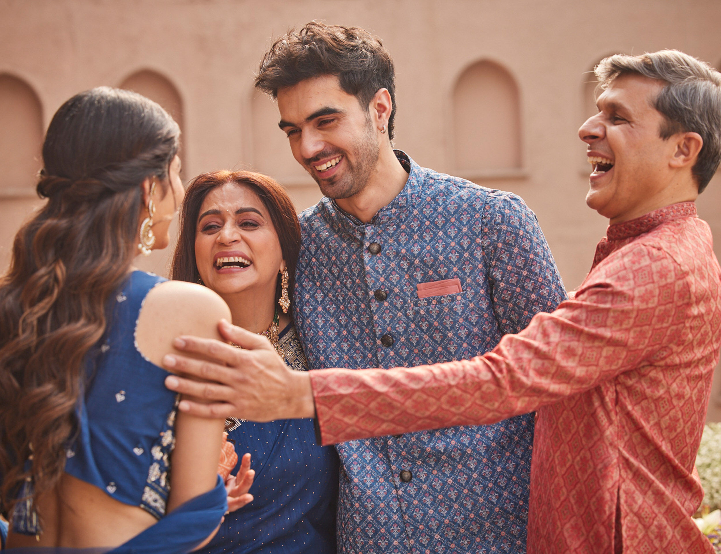 Joyful family members laughing and warmly embracing a guest at a Sikh Roka pre-wedding celebration.